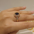 Gold ring with a blue gemstone on a person's finger against a neutral background