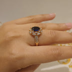 Gold ring with a blue gemstone on a person's finger against a neutral background
